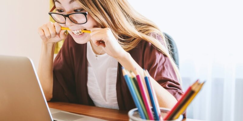 A woman wearing glasses is sitting at a desk with a laptop.