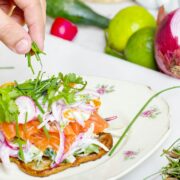 A person's hand sprinkling greens on a plate of food.