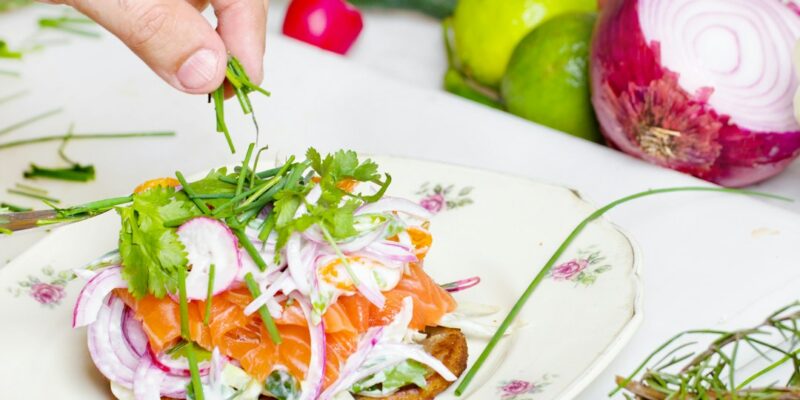 A person's hand sprinkling greens on a plate of food.