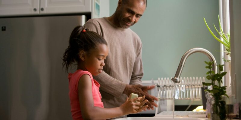 An african-american man and his daughter washing dishes in the kitchen.