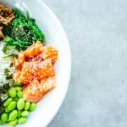 A bowl of asian food with vegetables and salmon.