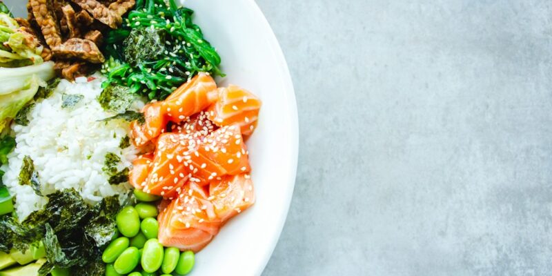 A bowl of asian food with vegetables and salmon.