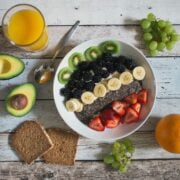 A bowl of fruit and a glass of orange juice on a wooden table.