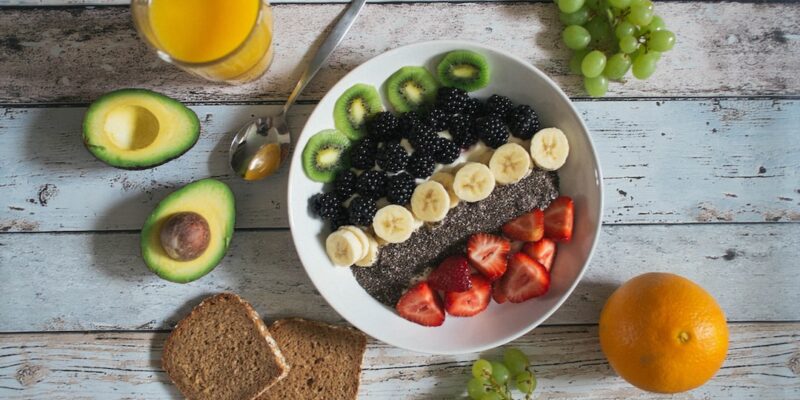 A bowl of fruit and a glass of orange juice on a wooden table.