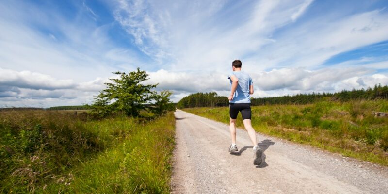 A man is jogging down a dirt road.