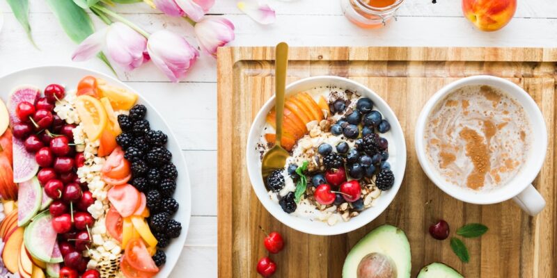 A bowl of fruit and a bowl of coffee on a wooden tray.