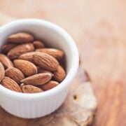 A bowl of almonds on a wood surface.