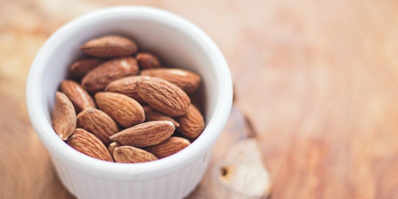 A bowl of almonds on a wood surface.