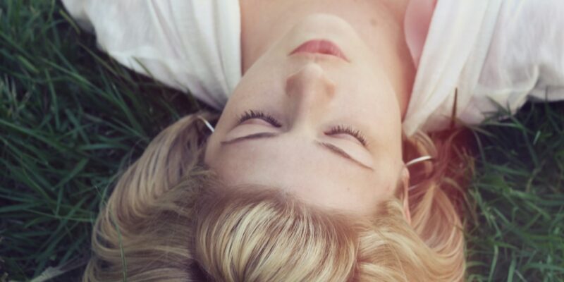 A woman laying in the grass with her eyes closed.