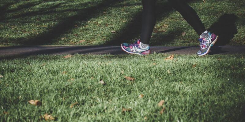 A woman is walking on the grass in a pair of running shoes.