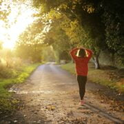 A woman walking on a road with trees and grass.