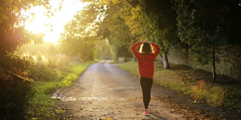 A woman walking on a road with trees and grass.