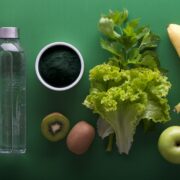 A bottle of water, fruit and vegetables on a green background.