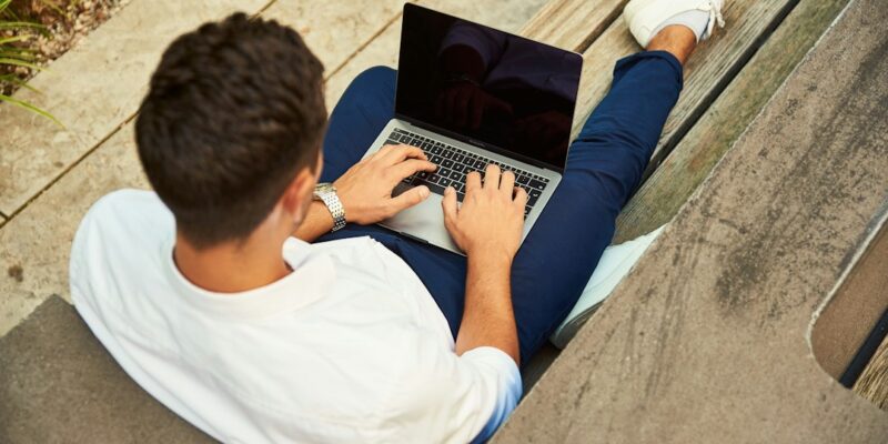 A man sitting on a bench using a laptop.