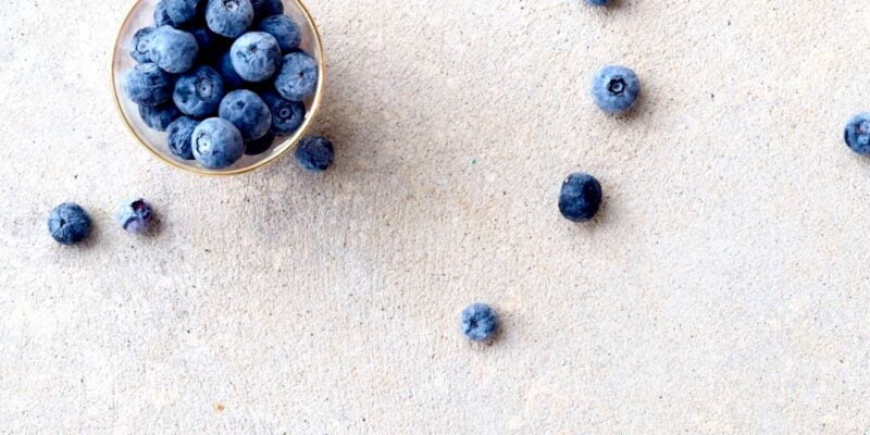 Blueberries in a bowl on a white surface.