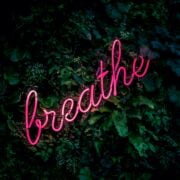 A pink neon sign with the word breathe in the background.