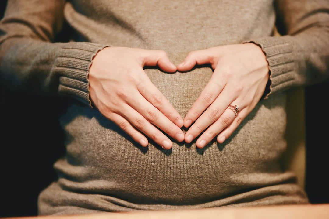 A pregnant woman making a heart shape with her hands.