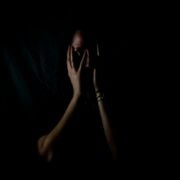 A woman with her hands covering her face in the dark.