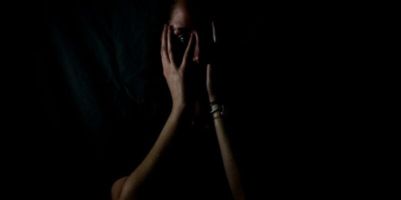 A woman with her hands covering her face in the dark.