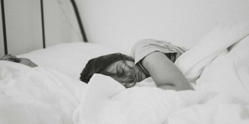 A black and white photo of a woman sleeping in bed.