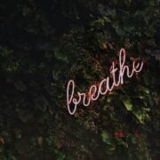 A neon sign with the word breathe in front of a green wall.