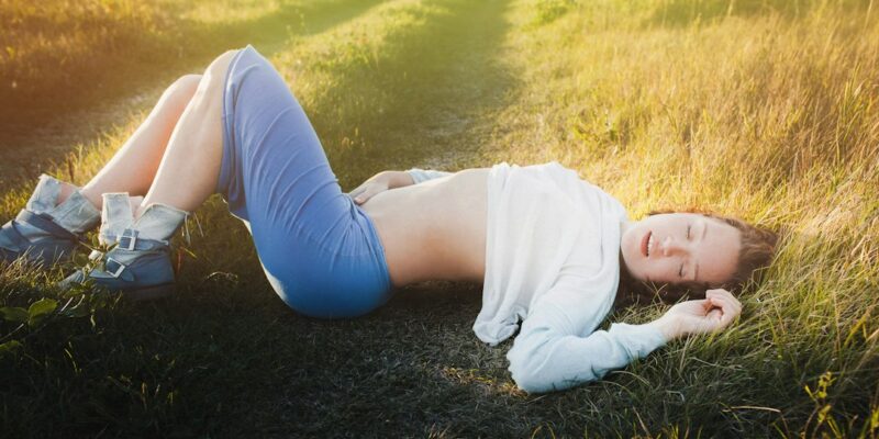 A young woman laying on the ground in a field.