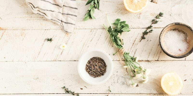 A bowl of herbs and lemons on a wooden table.