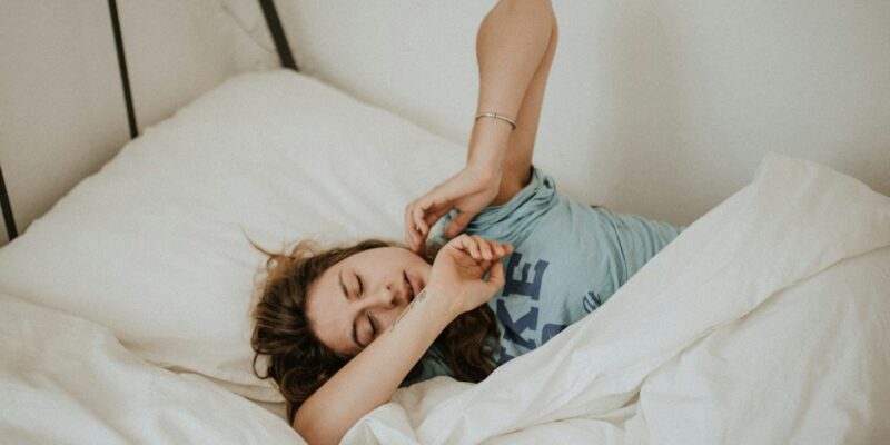 A woman laying in bed with her arms stretched out.