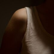 A woman in a white tank top standing in the dark.