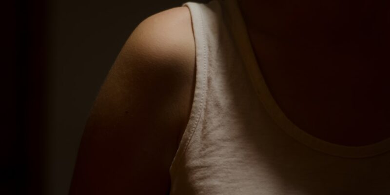 A woman in a white tank top standing in the dark.