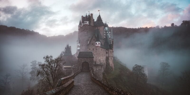 A castle sits on top of a hill in the fog.