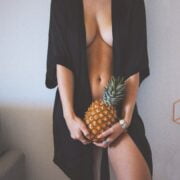 A woman in a black robe holding a pineapple.