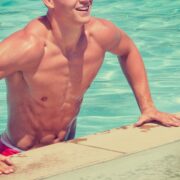 A man in swim trunks leaning on the edge of a pool.