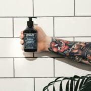 A tattooed man holding a bottle of body wash.