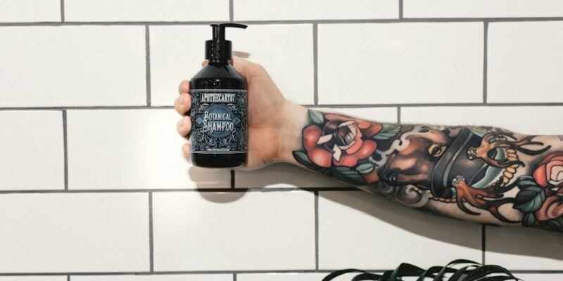 A tattooed man holding a bottle of body wash.