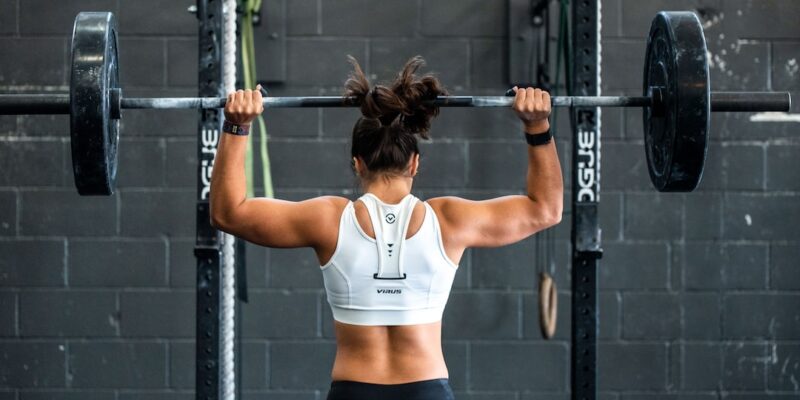 A woman lifting a barbell in a gym.