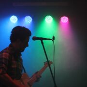 A man playing a guitar in front of colorful lights.