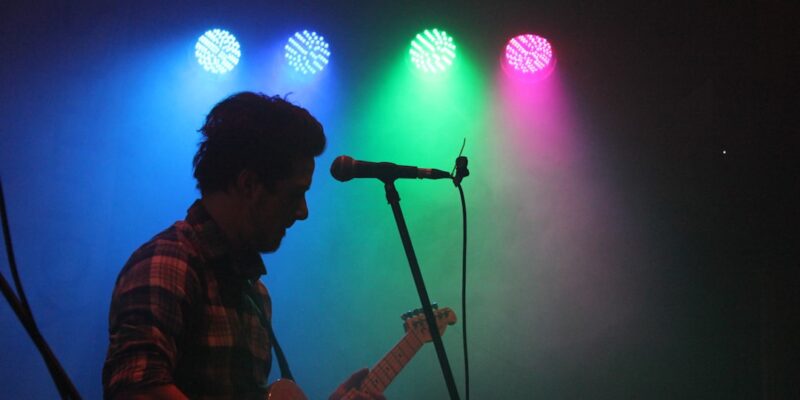 A man playing a guitar in front of colorful lights.