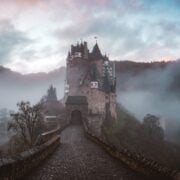 A castle sits on top of a hill in the fog.