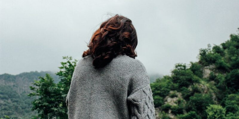 A woman is standing on a hill overlooking a forest.