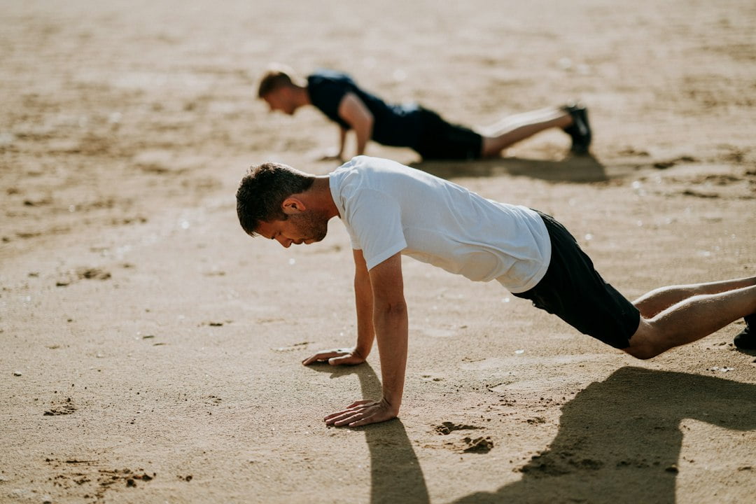 A man doing push ups on sand.