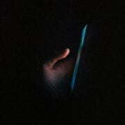 A hand illuminated by the glow of a smartphone screen in the dark.