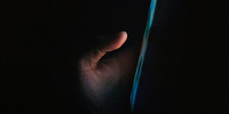 A hand illuminated by the glow of a smartphone screen in the dark.