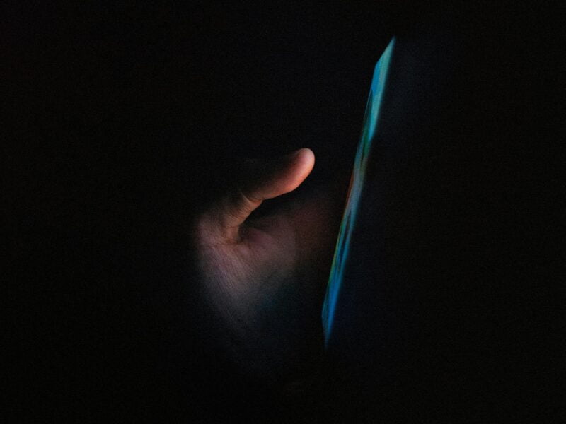 A hand illuminated by the glow of a smartphone screen in the dark.