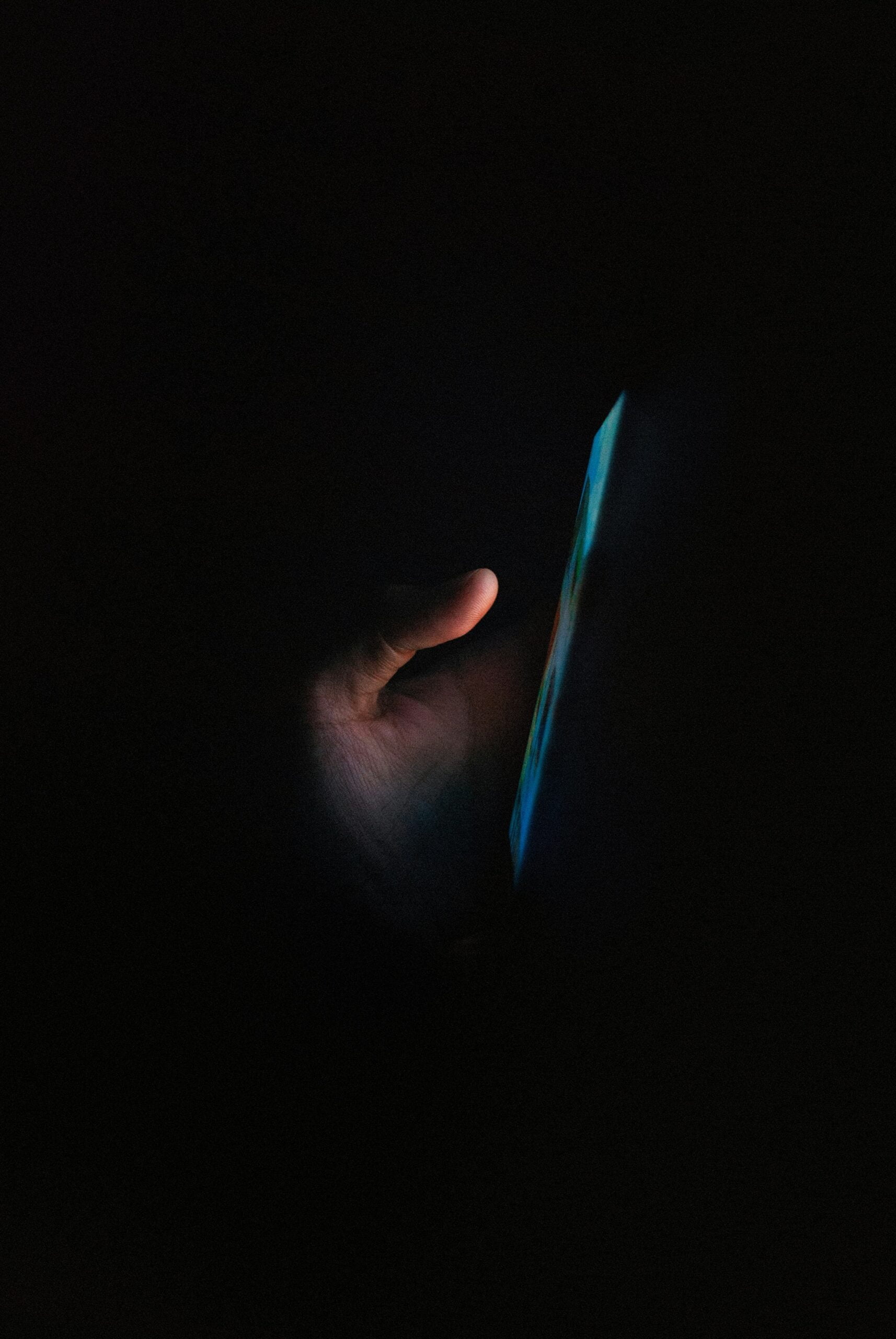 A hand illuminated by the glow of a smartphone screen in the dark.