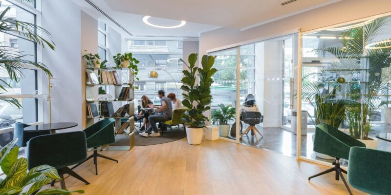 Modern cafe interior with customers, green plants, and stylish furniture.