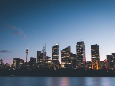 City skyline at dusk with illuminated buildings reflecting over water.