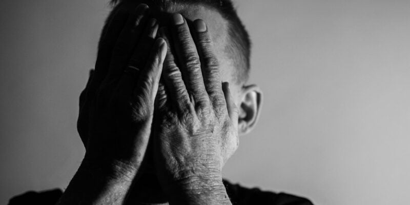 A black and white photo of a man covering his hands.