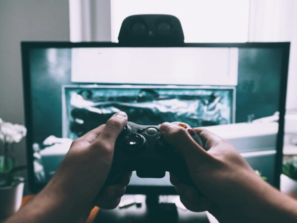 First-person perspective of a person playing a video game with a controller, in front of a monitor displaying the game's graphics.