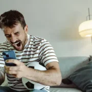 Man excitedly cheering while holding a smartphone and a game controller.